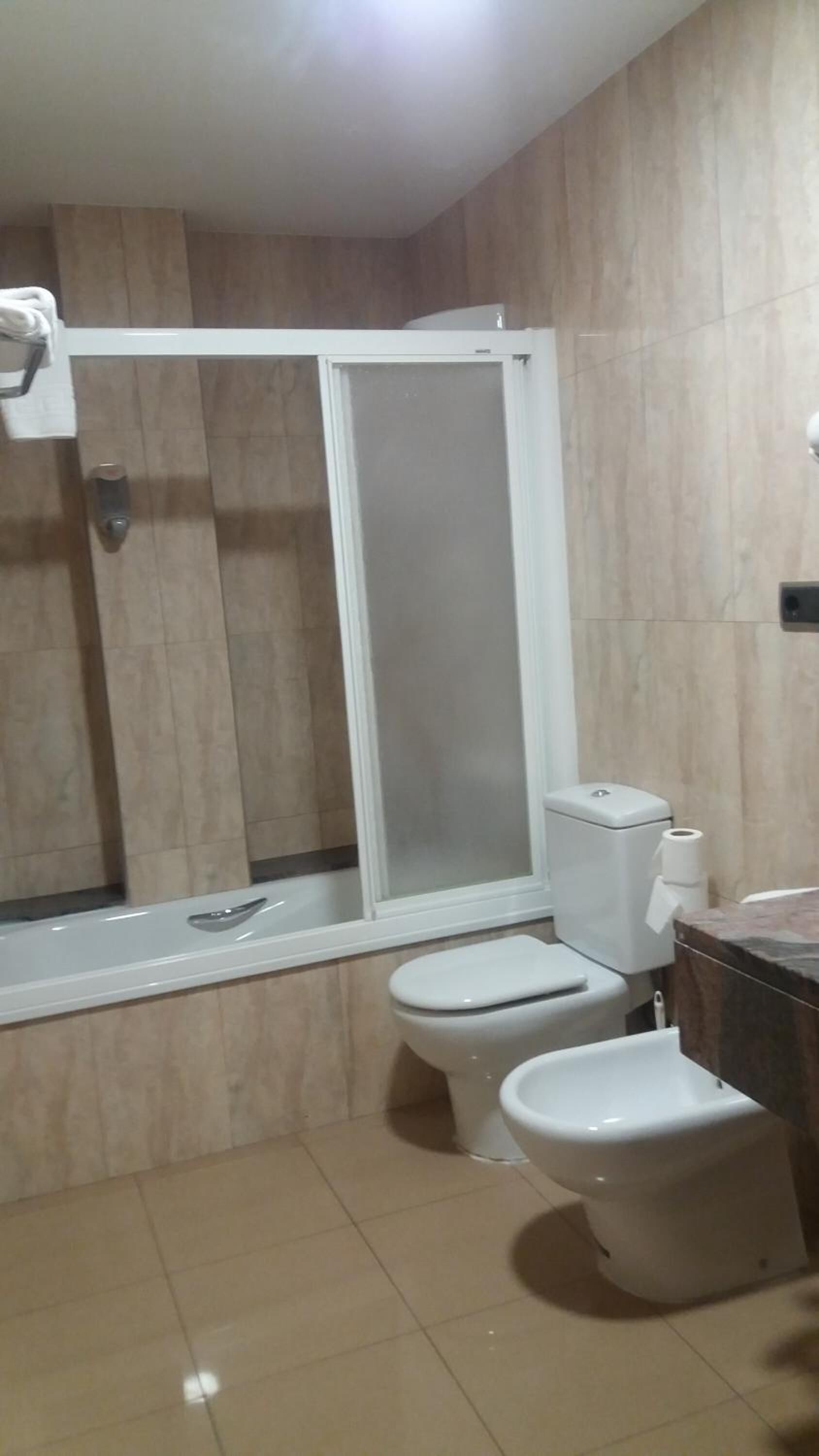 Un baño con ducha, dos inodoros y un lavamanos.