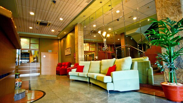 A lobby with a white sofa, red cushions, a large potted plant, and a reception desk. - Hotel Pio XII Jumilla (Jumilla)