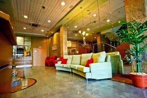 A lobby with a white sofa, red cushions, a large potted plant, and a reception desk. - Hotel Pio XII Jumilla (Jumilla)