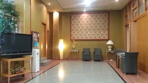 A hotel lobby with a flat-screen TV, a water dispenser, two chairs, a table, and a decorative wall panel. - Hotel Pio XII Jumilla (Jumilla)