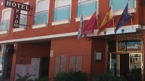 A hotel building with a red facade, multiple balconies, and flags including the European Union flag. - Hotel Pio XII Jumilla (Jumilla)