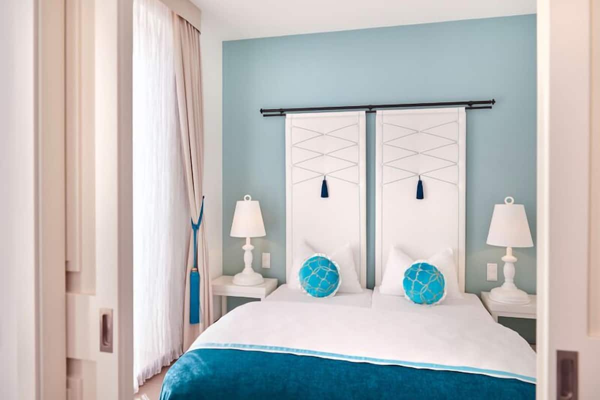 Een hotelkamer met een bed, twee nachtkastjes, een raam met gordijnen en een blauwe muur.