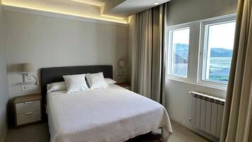 A hotel room with a large bed, bedside tables, a nightstand, a window with a view, and a ceiling light.