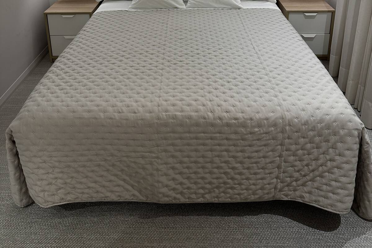 Una cama bien hecha con un edredón acolchado, dos mesitas de noche con lámparas y un cabecero.