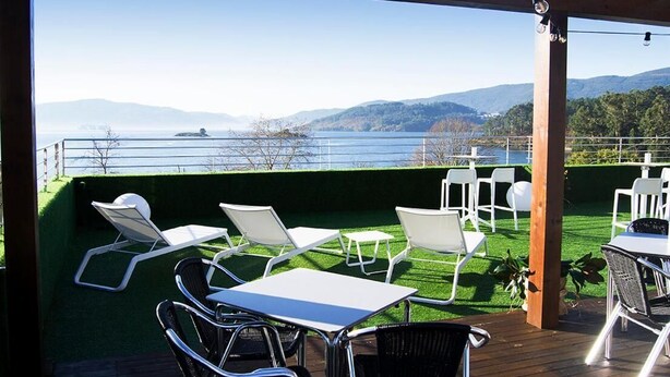 A terrace with white chairs and tables, overlooking a lake and hills.