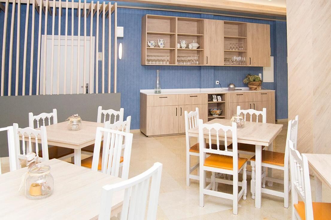 Un comedor con mesas y sillas de madera blanca, una cocina con armarios de madera clara y una pared de acento azul.