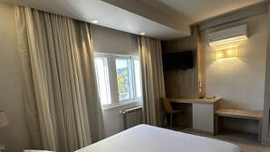 A hotel room with a bed, a desk, a chair, a TV, and a window with curtains.