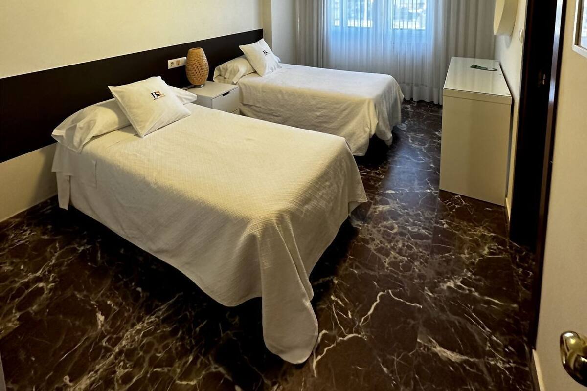 Habitación de hotel con dos camas, un escritorio, un televisor de pantalla plana y una lámpara en el techo.