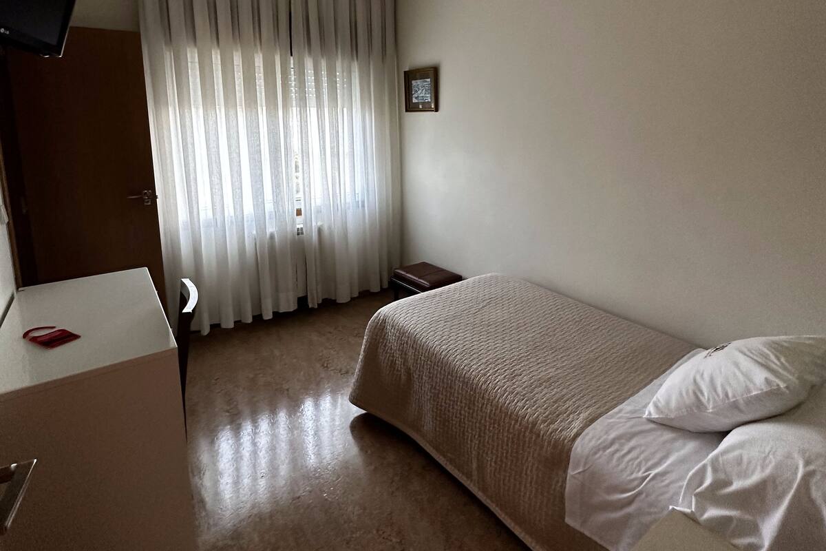 Una habitación de hotel con cama, escritorio, televisor y ventana con cortinas.