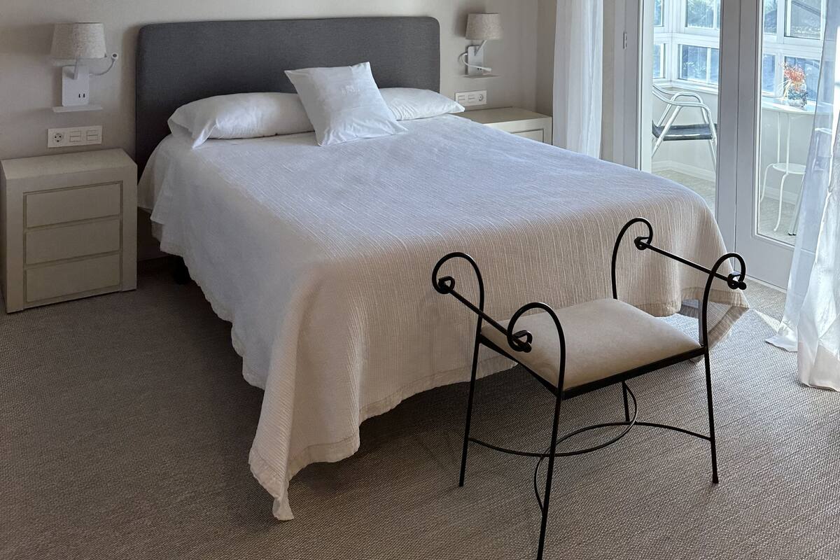 Una habitación de hotel con cama, mesitas de noche, una silla y vistas al exterior.