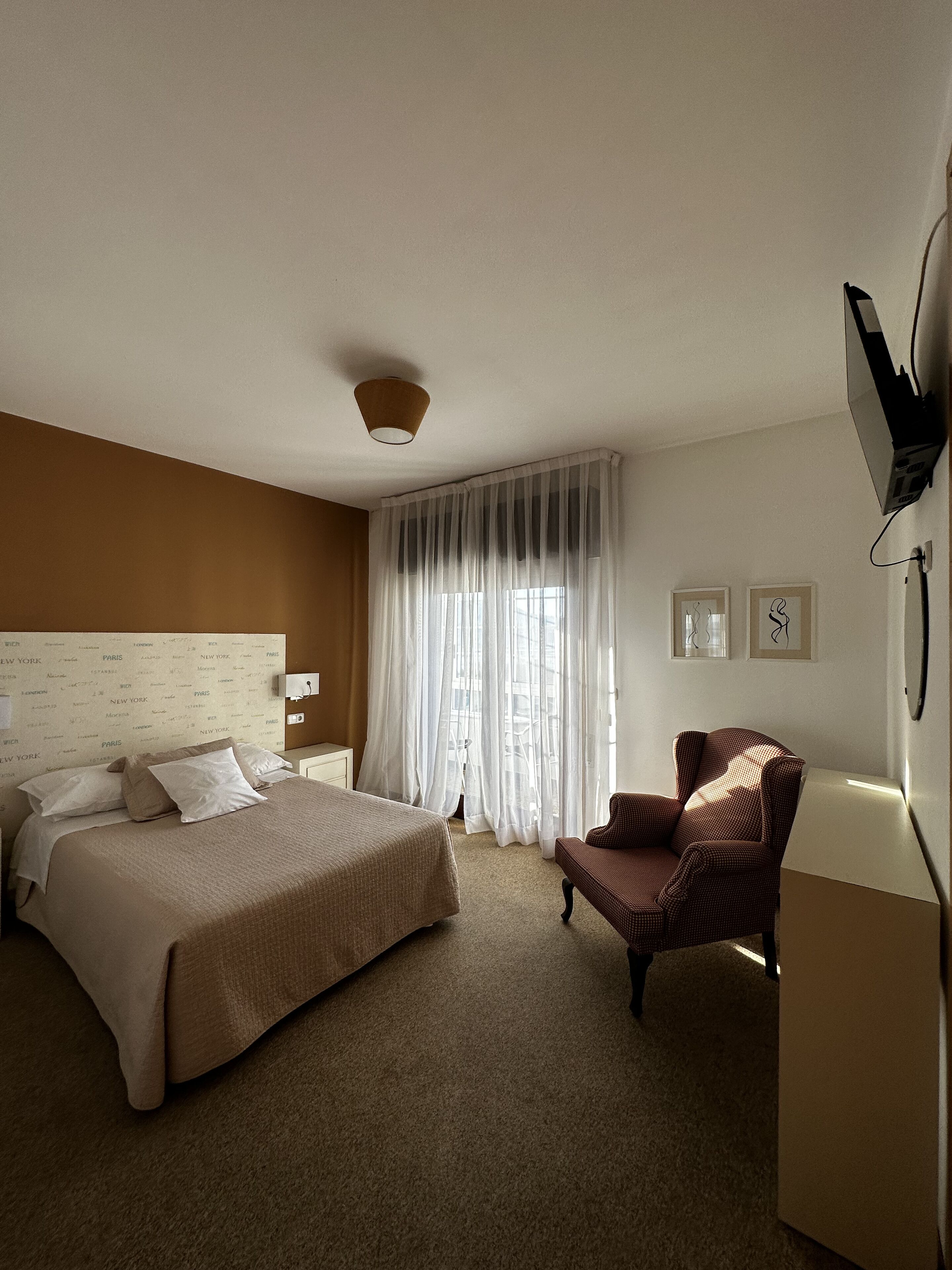 Een hotelkamer met een groot bed, een stoel, een bureau en een aan de muur bevestigde televisie.