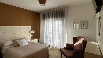 Een hotelkamer met een groot bed, een stoel, een bureau en een aan de muur bevestigde televisie.