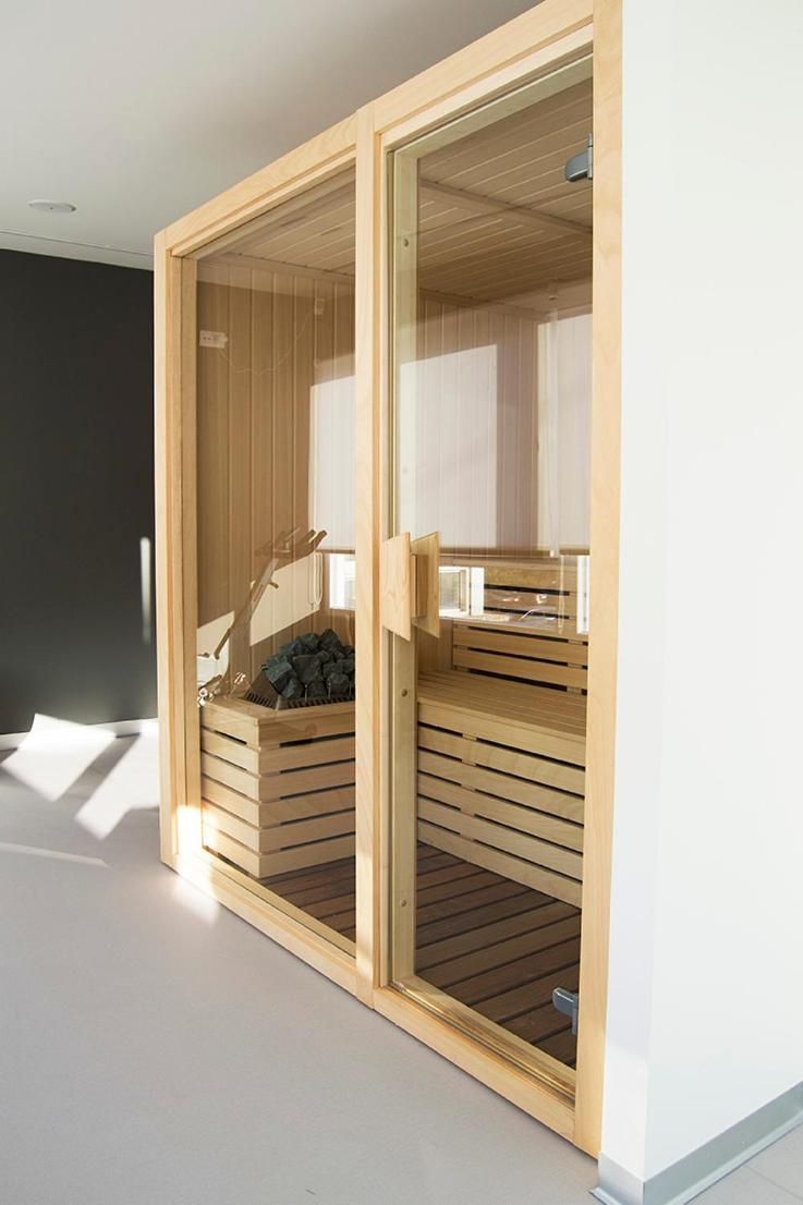 Una sauna de madera moderna con puerta de cristal, un banco y una pila de troncos.