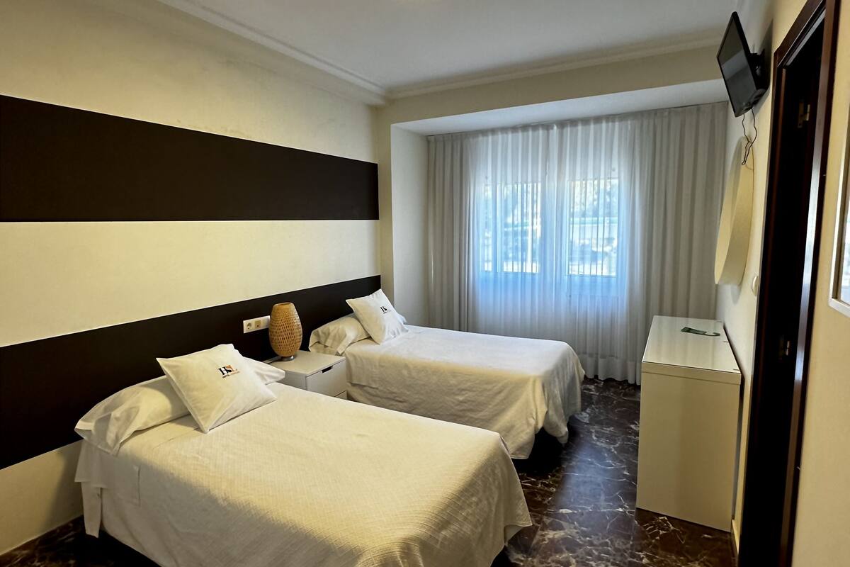 Habitación de hotel con dos camas, un escritorio, un televisor y una ventana con cortinas.