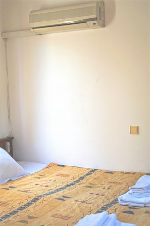 Una habitación con una cama, aire acondicionado, una mesita de noche y un enchufe.