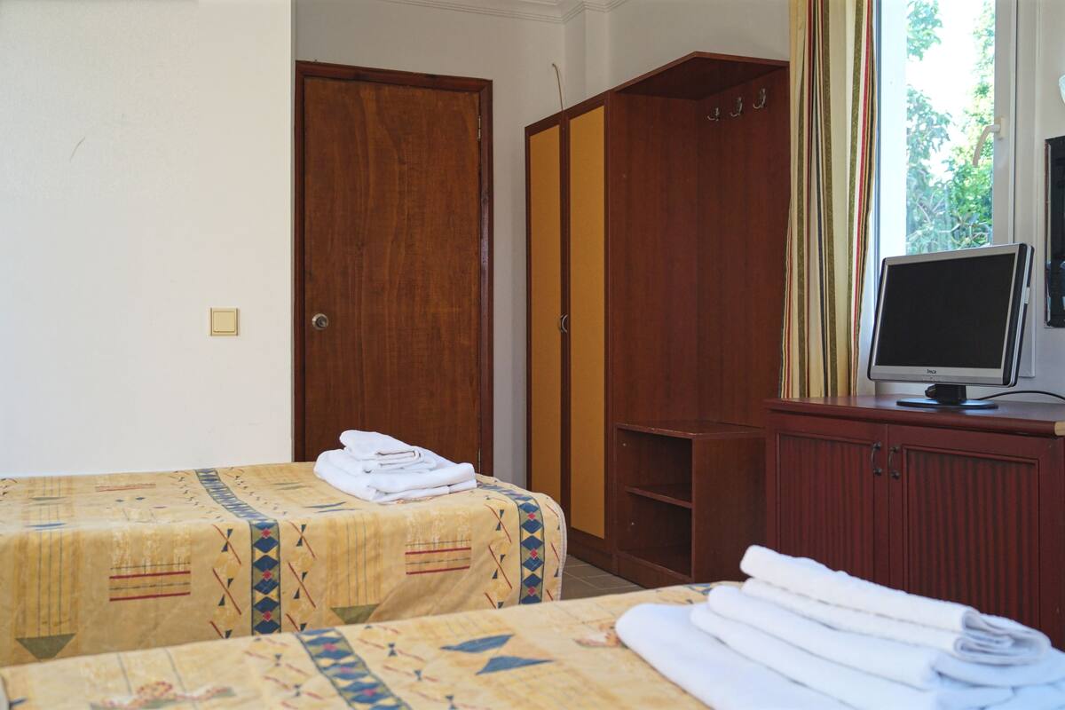 A hotel room with two beds, a wardrobe, a television, and a window with curtains.
