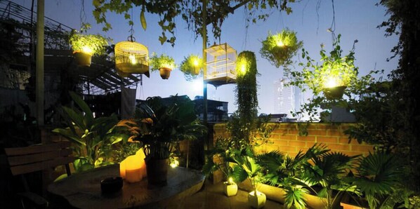 An outdoor patio area with tables and chairs, surrounded by potted plants and hanging planters.