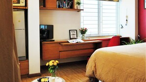 A bedroom with a bed, a desk, a television, and a window with curtains.
