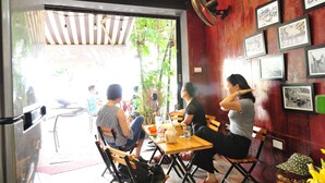 A restaurant with wooden tables and chairs, framed pictures on the wall, and a fan on the ceiling.