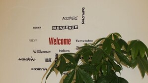 A potted plant with a sign above it displaying "Welcome" and various other words in different languages. - MyRoom CenterStation (Bologna)