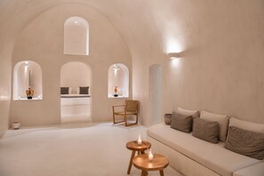 A minimalist room with a large bed, a wooden chair, a sofa, and two small tables with candles.