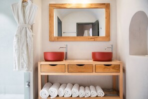A bathroom with a wooden vanity, two red sinks, a mirror, and neatly rolled towels.