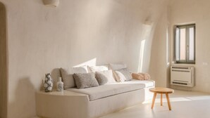 Ett minimalistiskt vardagsrum med en vit soffa, en liten träpall och ett element.