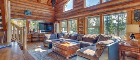L’intérieur d’une cabane en rondins, avec un grand canapé, une table basse en bois et un téléviseur placé dans un coin.