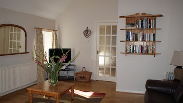 Una sala de estar con televisor, estantería y un florero con flores sobre una mesa.