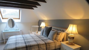 A bedroom with a bed, two bedside tables with lamps, a chair, a desk with a mirror, and a window. - Harleyburn Cottages (Melrose)