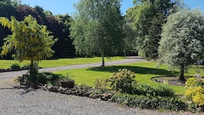 A well-maintained garden with a variety of trees, a gravel path, and neatly trimmed grass. - Harleyburn Cottages (Melrose)