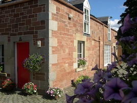Un edificio de piedra con una puerta roja, ventanas con macetas de flores y un sendero de ladrillo.