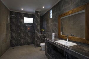 Un baño moderno con pared de mármol, un espejo grande, ducha y lavamanos.