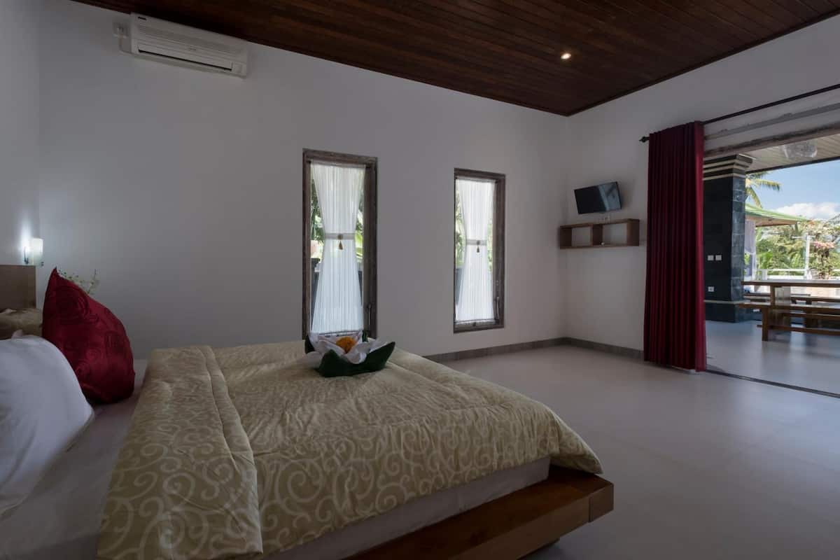 A bedroom with a bed, two windows, a TV, and a view of the outdoors.