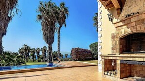 A pool with a clear blue sky, palm trees, and a stone fireplace. - Serenity by the Green (Adeje)