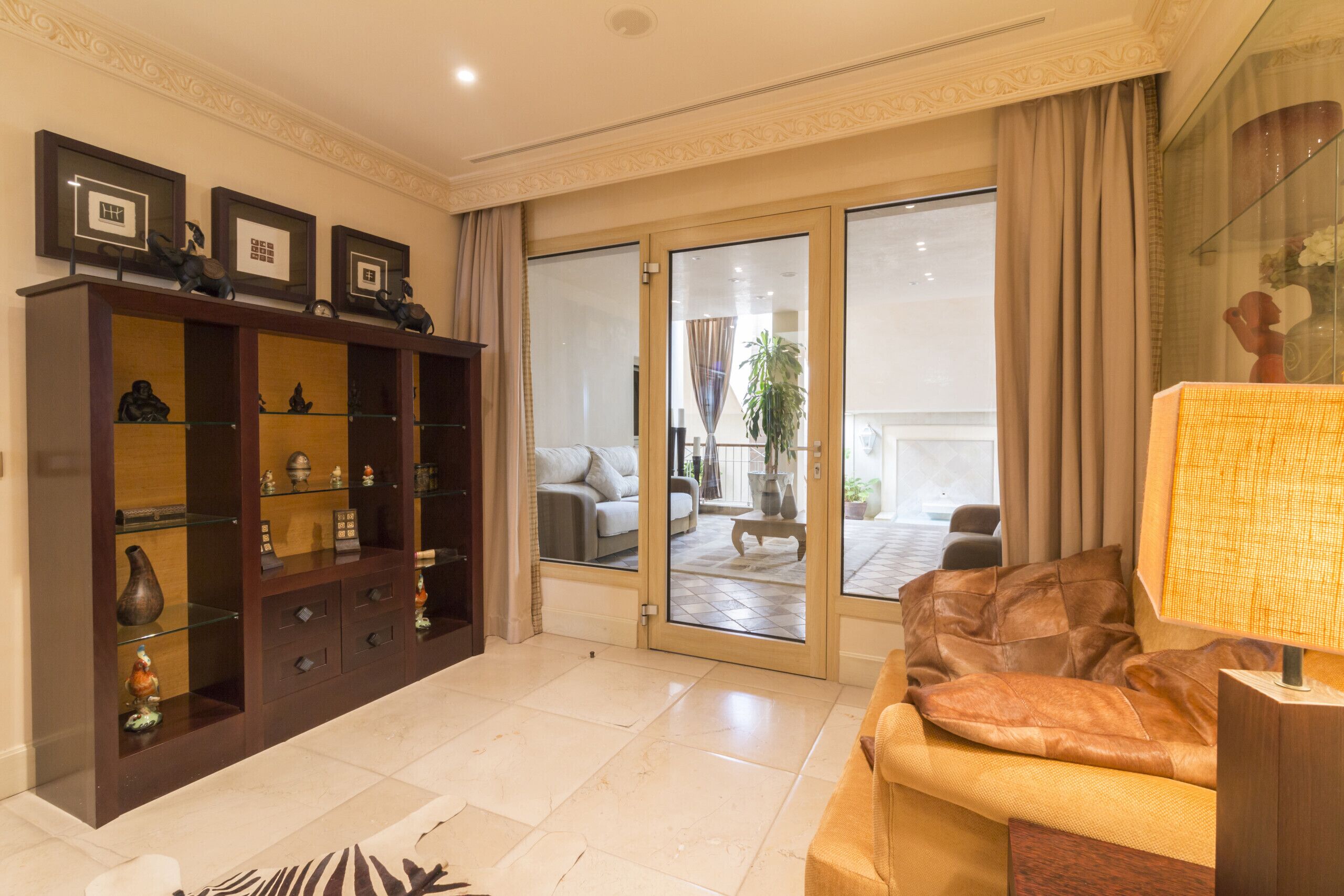 A spacious living area with a sofa, a wooden cabinet with glass doors, and a sliding glass door leading to an outdoor patio.