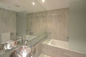 Ein modernes Badezimmer mit zwei Waschbecken, einem Glaswaschtisch, einer Badewanne und einem großen Spiegel.