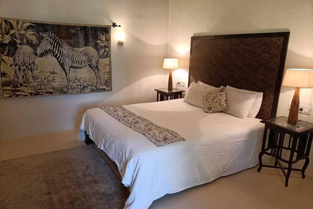 A bedroom with a large bed, two bedside tables with lamps, a rug, and a wall painting of zebras.