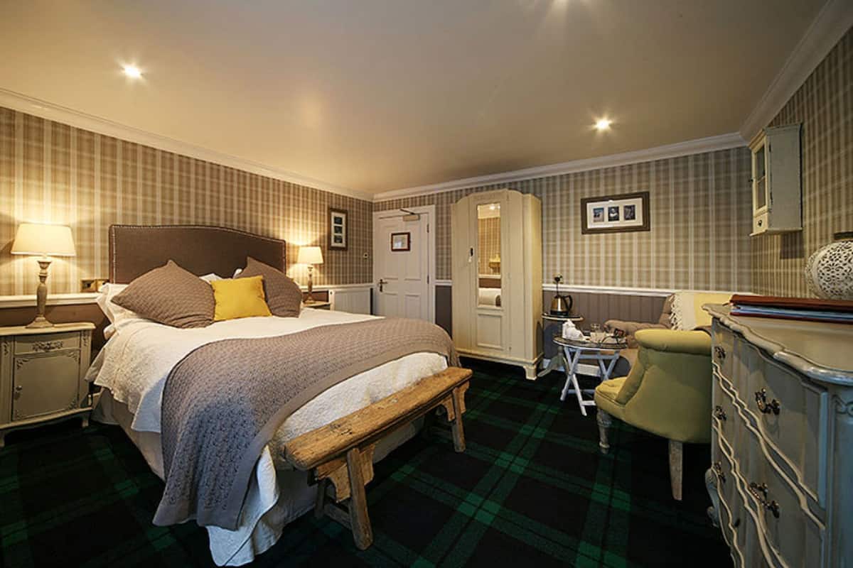A traditional hotel room with a large bed, a bench, a dresser, a chair, and a mirror.