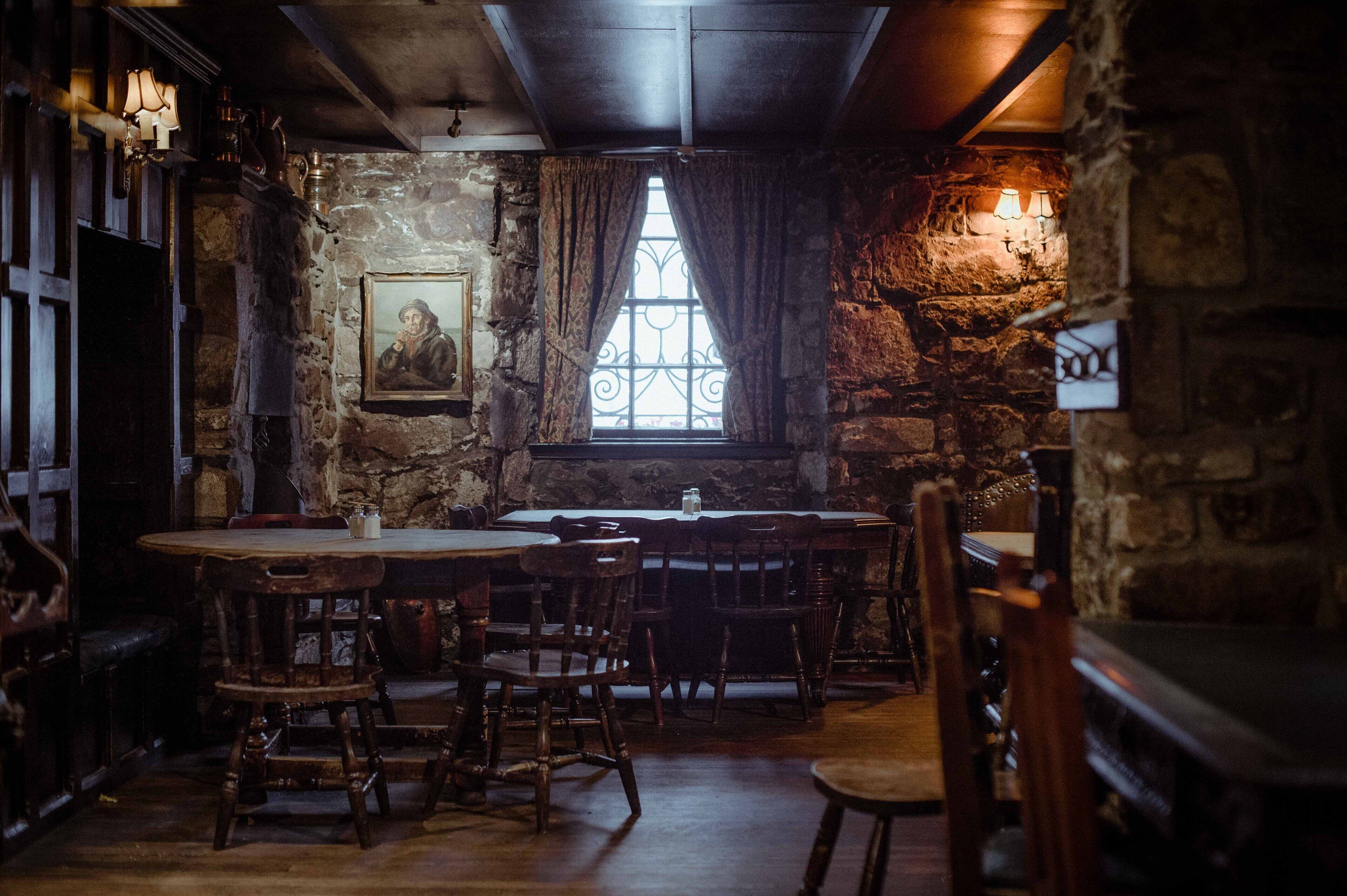 A rustic interior with stone walls, wooden furniture, and a large window with curtains.