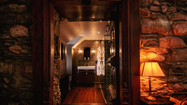 A narrow stone-walled hallway leading to a bathroom with a wooden floor, a sink, and a robe hanging on a rack. - The George Hotel (Inveraray)