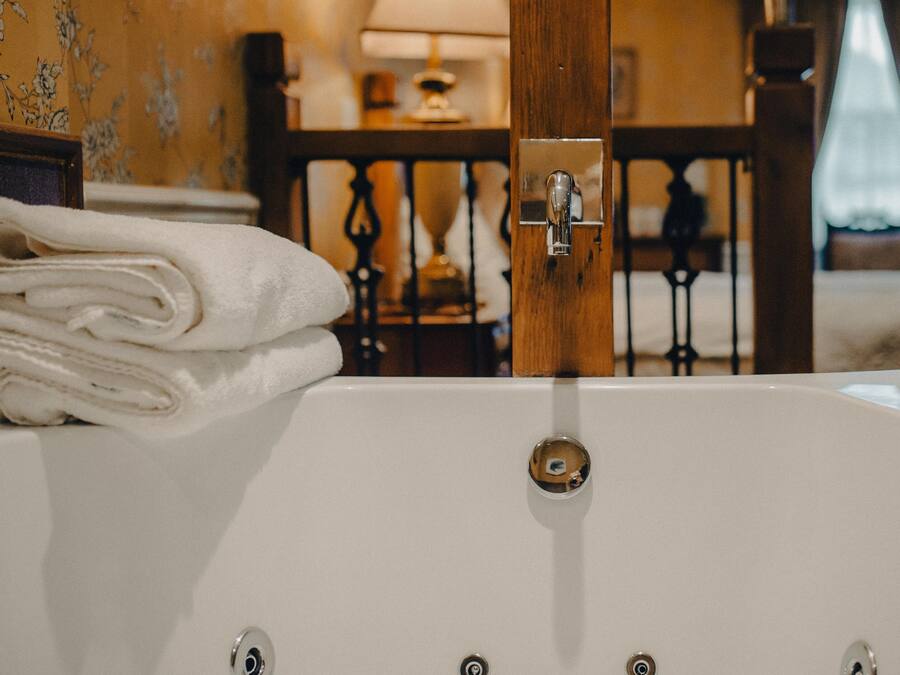 A white bathtub with a wooden door handle, a towel stack, and a wooden railing in the background.