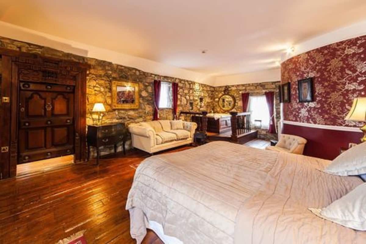A bedroom with a large bed, a stone wall, a wooden door, and a red patterned wall.
