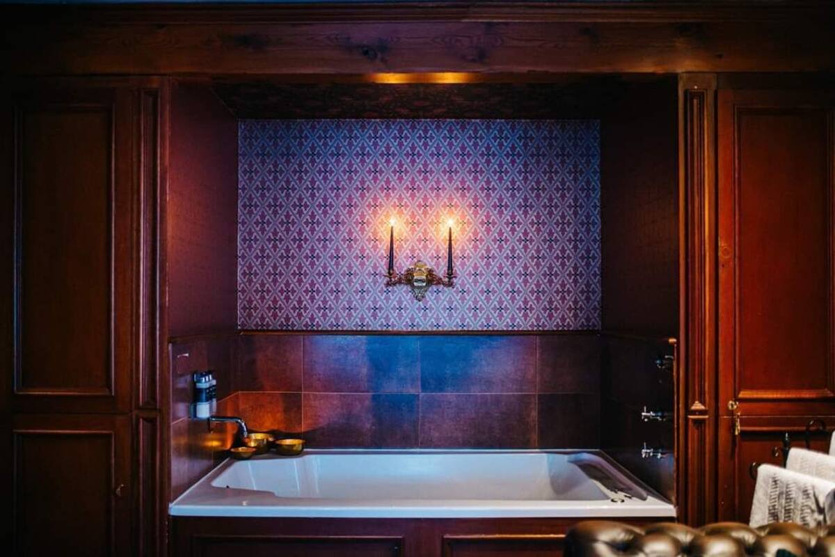 A bathroom with a large bathtub, a patterned wall, and two candles on the wall.