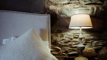 A bed with a headboard and a lamp against a stone wall.