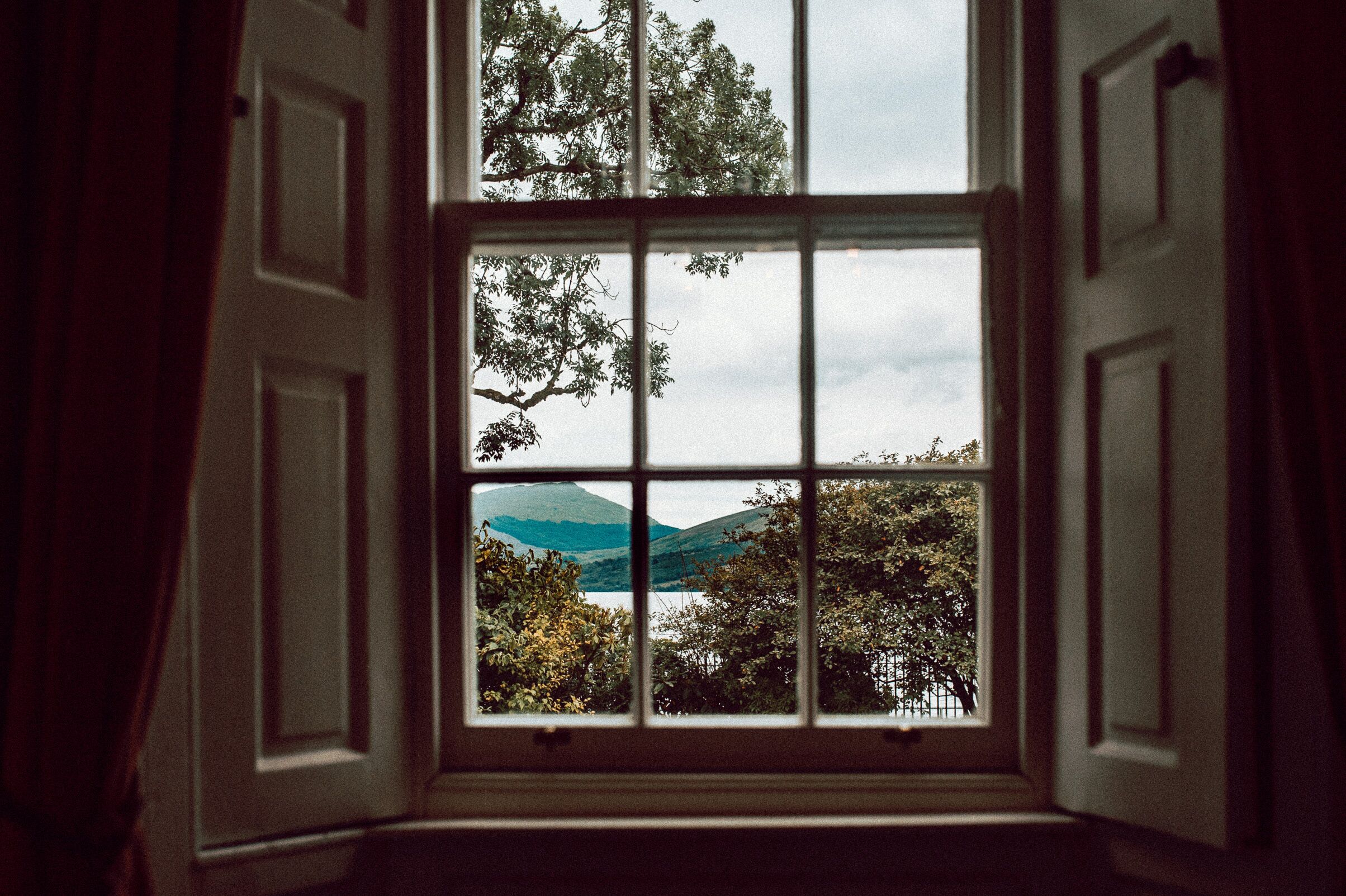 An open window with a view of trees and hills.