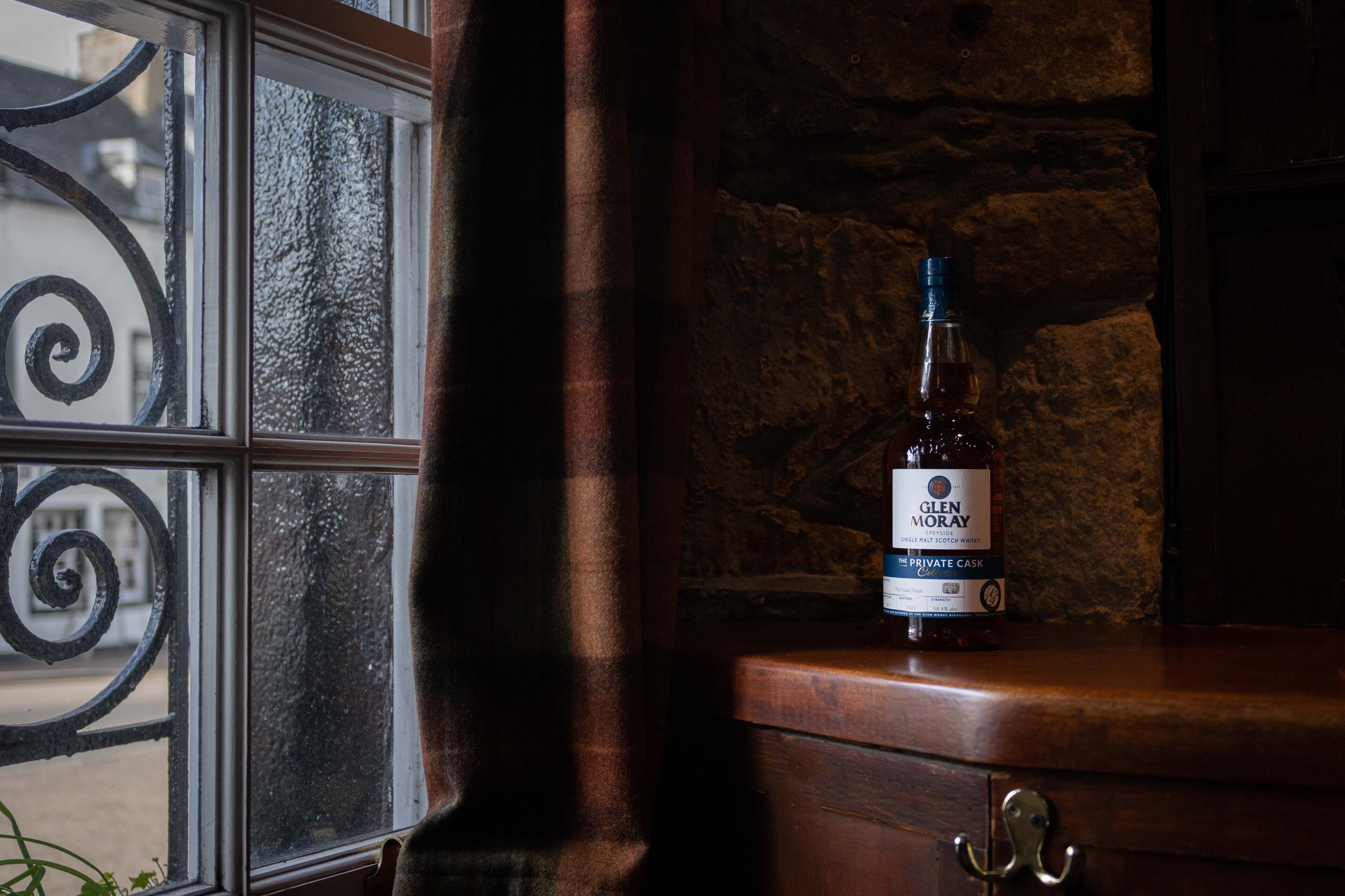 A bottle of Glenmorangie whisky on a wooden surface near a window with a metal grill.