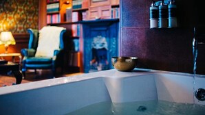 A bathtub with a metal bowl, a chair, and a bookshelf in the background. - The George Hotel (Inveraray)