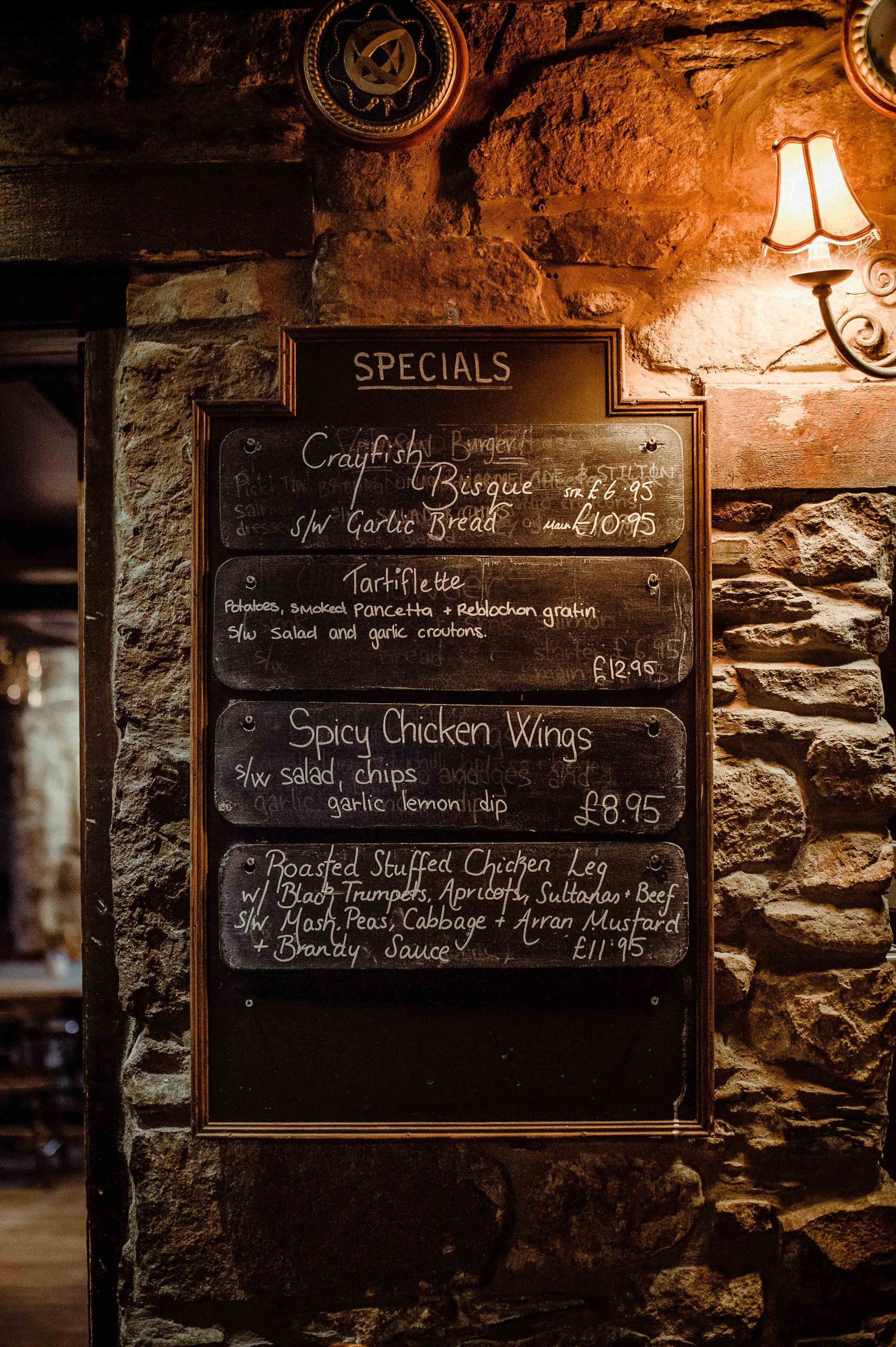 A chalkboard menu listing specials such as crayfish, tartiflette, spicy chicken wings, and roasted stuffed chicken leg.