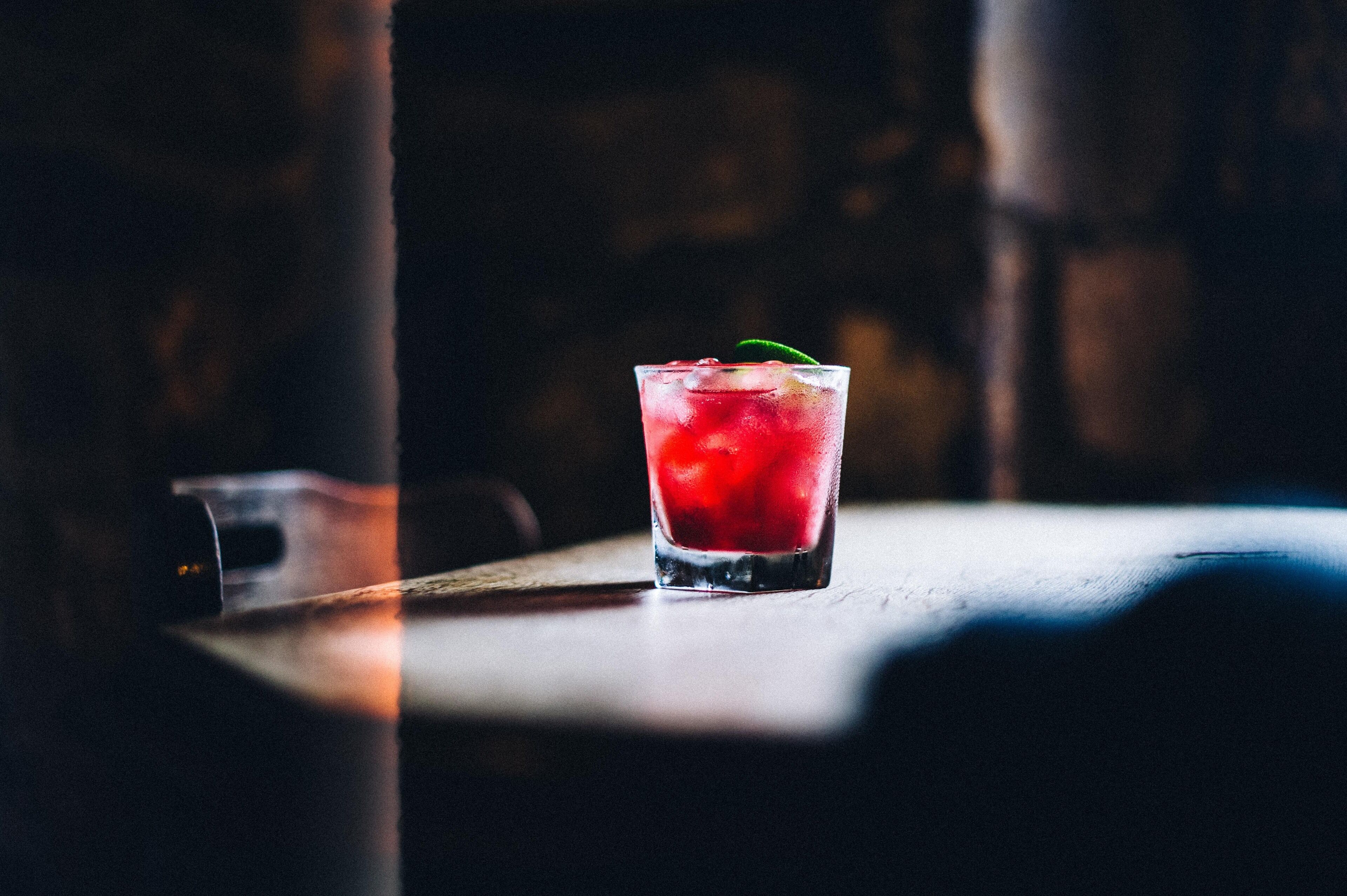 A glass of red beverage on a table with a blurred background.